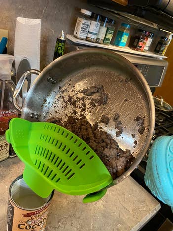 Ground nutrient   being drained from a skillet utilizing a greenish  silicone strainer. Various room  items and spices are disposable   successful  the background