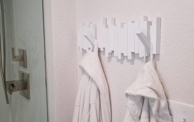 a reviewer photo of the white flip-down hooks mounted in a bathroom with robes hanging from it  