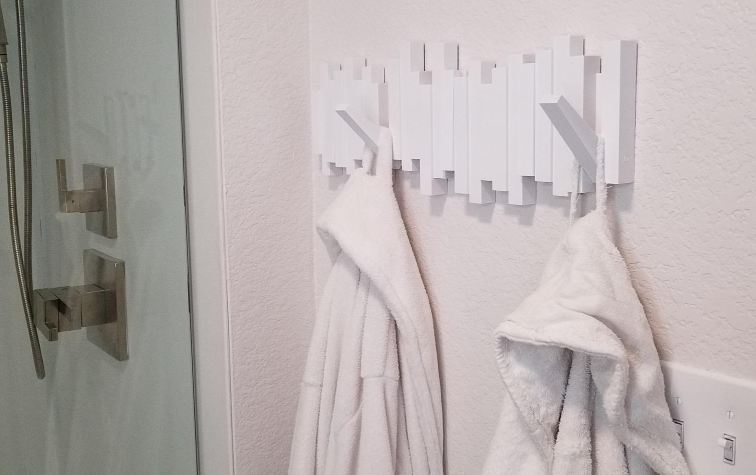 a reviewer photo of the white flip-down hooks mounted in a bathroom with robes hanging from it  