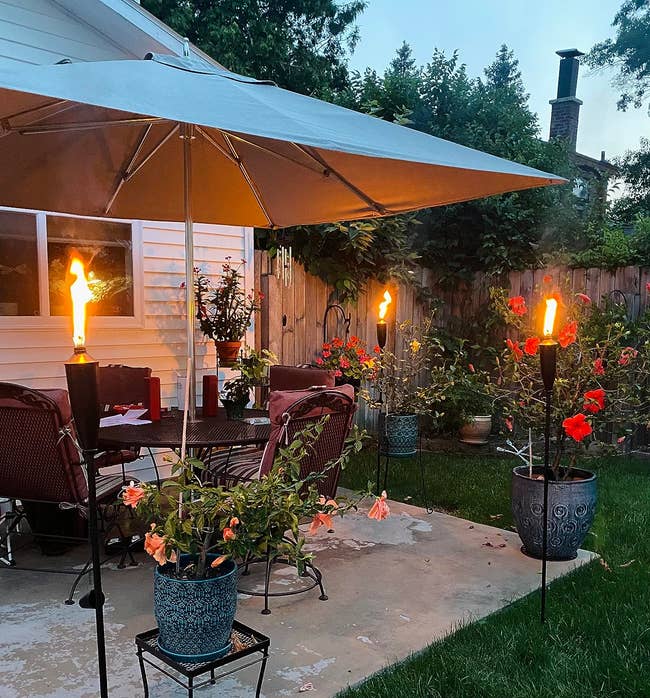 Backyard patio with umbrella, chairs, and tiki torches astatine dusk