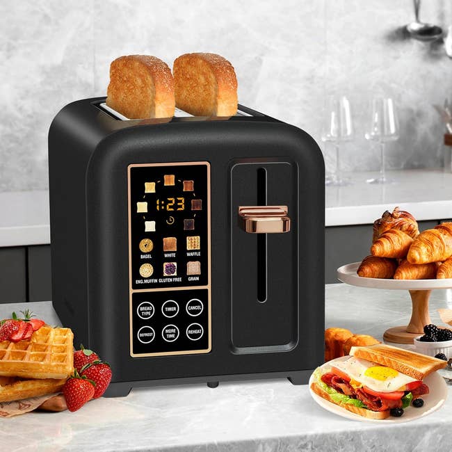 Modern toaster with digital display and multiple settings on a kitchen counter, surrounded by various breakfast foods