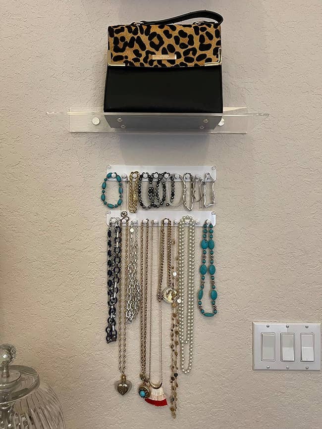 A reviewer's wall-mounted jewelry organizer with various necklaces hanging and a leopard print clutch on top shelf