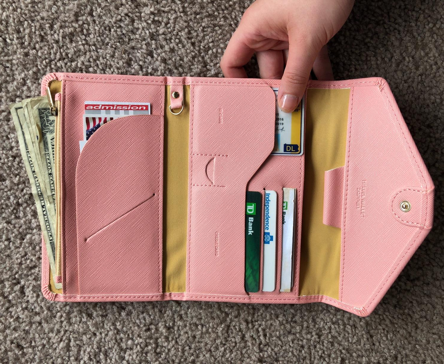 reviewer holding the opened pink wallet full of cards, cash, ids, and tickets