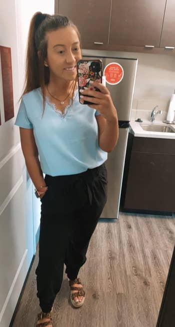 Woman poses in a casual outfit with a T-shirt and pants, taking a mirror selfie in a kitchen setting