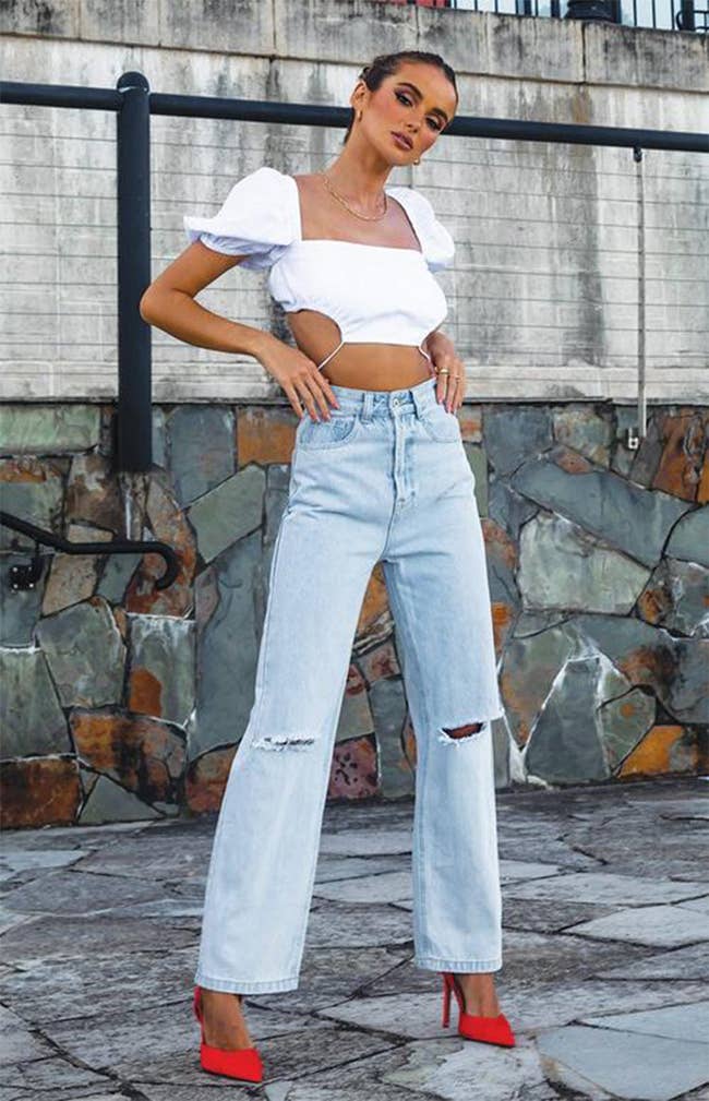 model in light wash jeans with rips at knees with crop top and heels