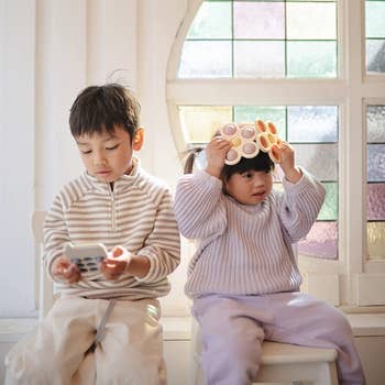 two kids holding rubber bubble toys. one is a phone and one is flowers. 