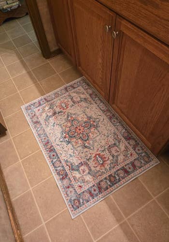 Decorative patterned rug placed on a tiled kitchen floor near wooden cabinets