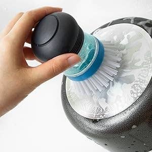 Hand holding a crockery  scrubber with a soap dispenser, cleaning a cookware  