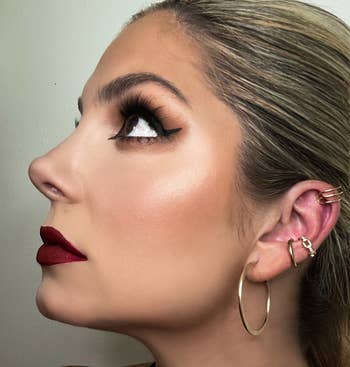 Reviewer with bold makeup, including melodramatic  eyelashes and reddish  lipstick, wearing hoop and receptor  cuff earrings