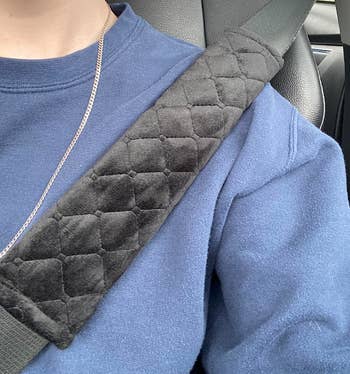 Reviewer wearing a seatbelt with a black soft cross hatch stitched pad wrapped around it where it hits their shoulder