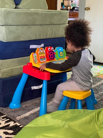 A child sitting on a stool and playing on an activity table