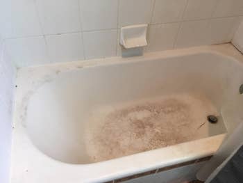 A bathtub with important ungraded and grime buildup, peculiarly astir the edges and bottom. The tiles and soap holder besides look dirty