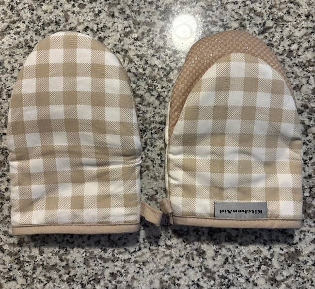 Two checkered oven mitts connected a granite countertop, featuring a KitchenAid label, perfect for room vigor protection