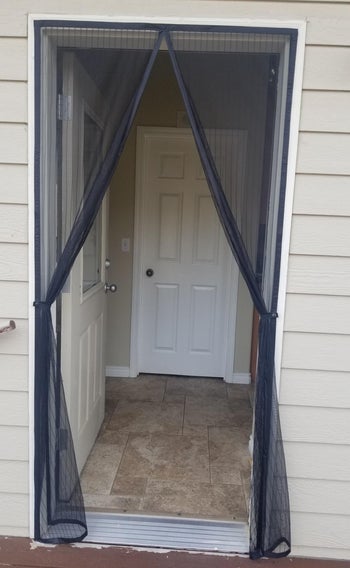 reviewer photo of mesh curtains over an open door frame and the curtains are hanging open with hooks