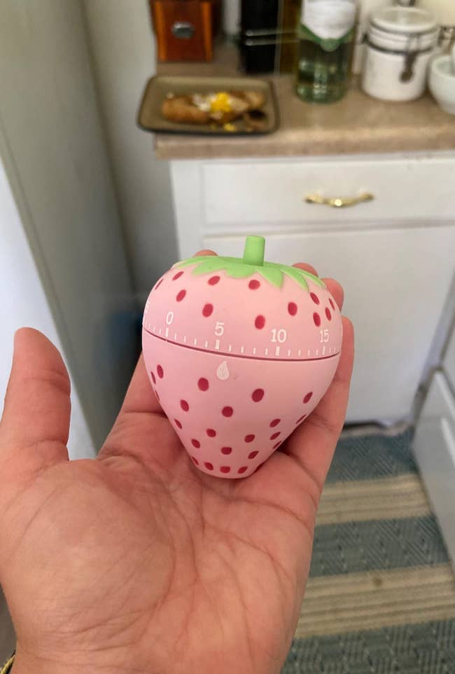 Hand holding a strawberry-shaped room timer, with infinitesimal markings visible, successful a room setting