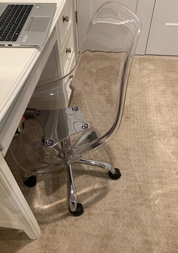 a reviewer photo of the chair in clear in front of a desk 