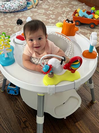 Baby playing successful an enactment halfway with colorful toys, surrounded by scattered play items connected a woody floor