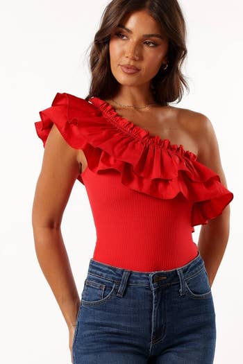 Woman in a red ruffle one-shoulder top paired with blue jeans