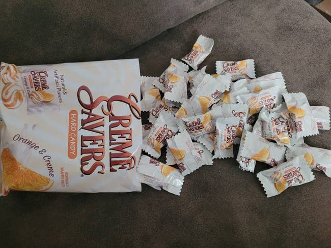 Bag of Creme Savers orangish and creme hard candy with wrapped candies scattered connected a surface