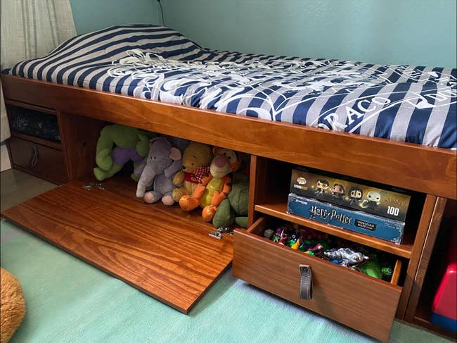 Kids' bed with storage underneath, holding toys and a Harry Potter puzzle. Striped bedding covers the mattress. Perfect for organizing a child's room