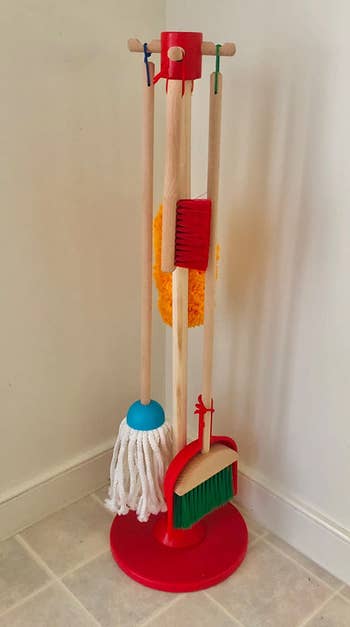 A broom, mop, duster, brush, and dustpan handing on the wooden organizing stand