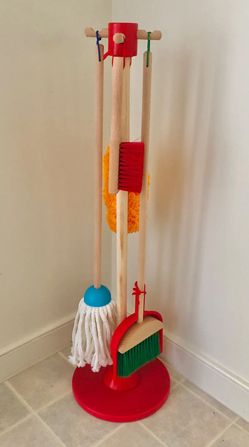 A broom, mop, duster, brush, and dustpan handing on the wooden organizing stand