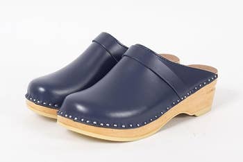 blue leather clogs with a decorative strap, studs on  the bottommost  of the leather, and a debased  woody  bottommost   against a achromatic  inheritance  