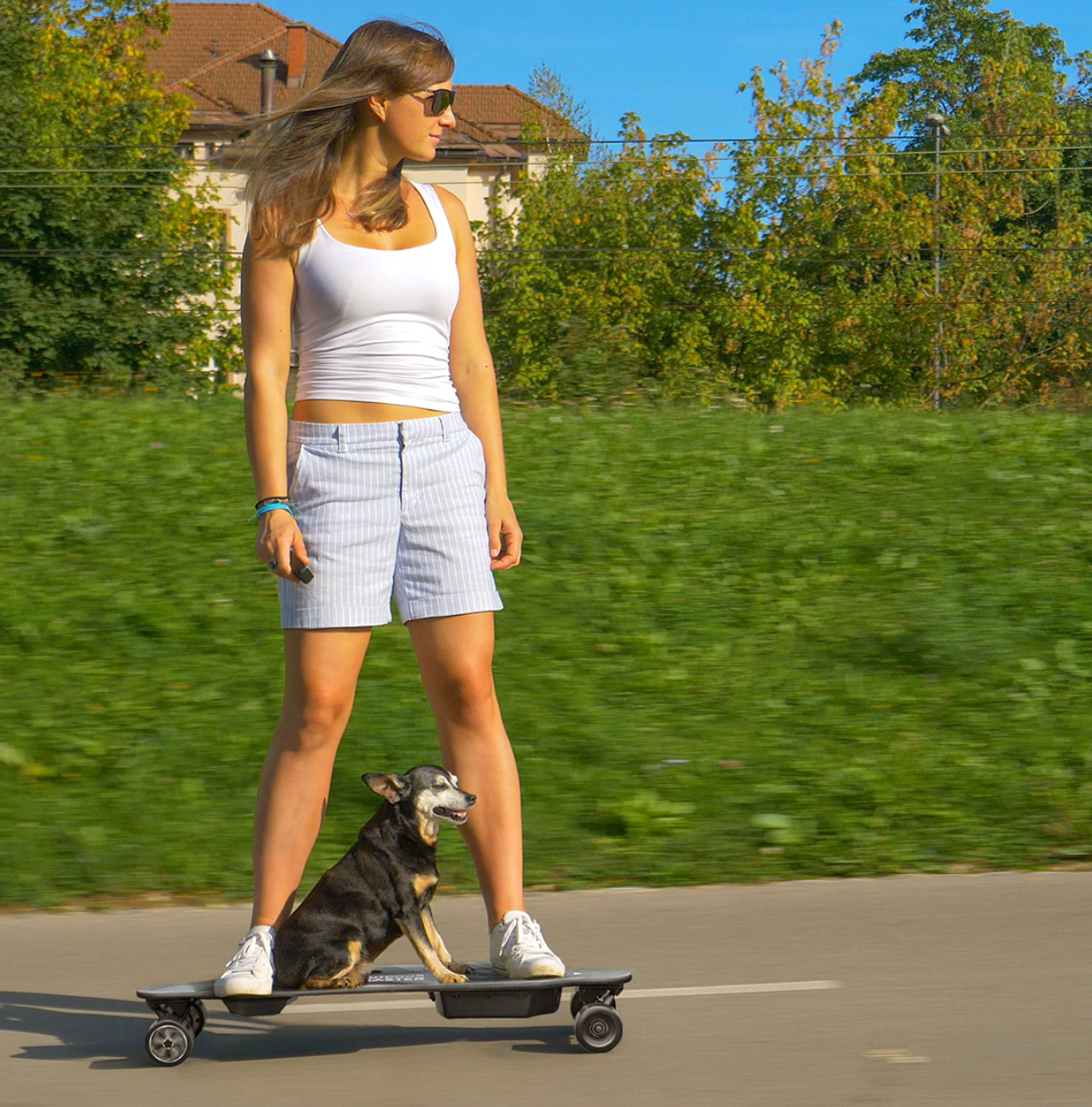 Model is on a longboard with their dog in the middle of the board as well while cruising down the road