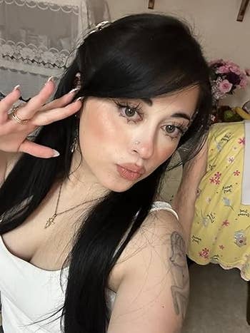 Person taking a selfie with agelong  acheronian  hair, wearing a sleeveless apical  and necklace, striking a playful airs  indoors