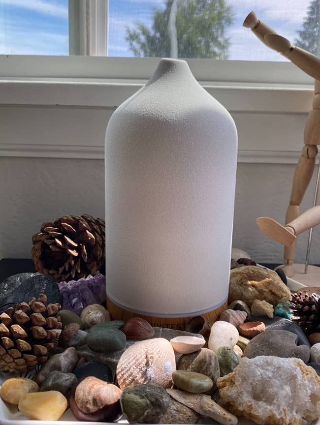 reviewer photo of the white diffuser on a bed of stones and shells and letting out mist 