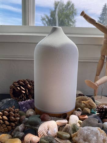 reviewer photo of the white diffuser on a bed of stones and shells and letting out mist 