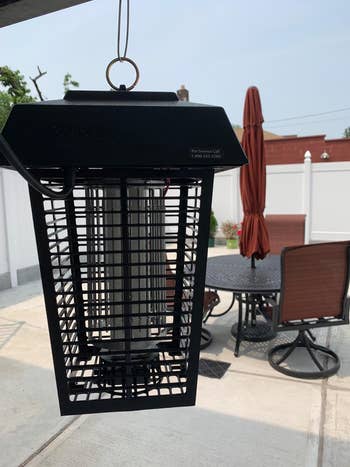 Outdoor electric bug zapper hanging on a patio with furniture in the background