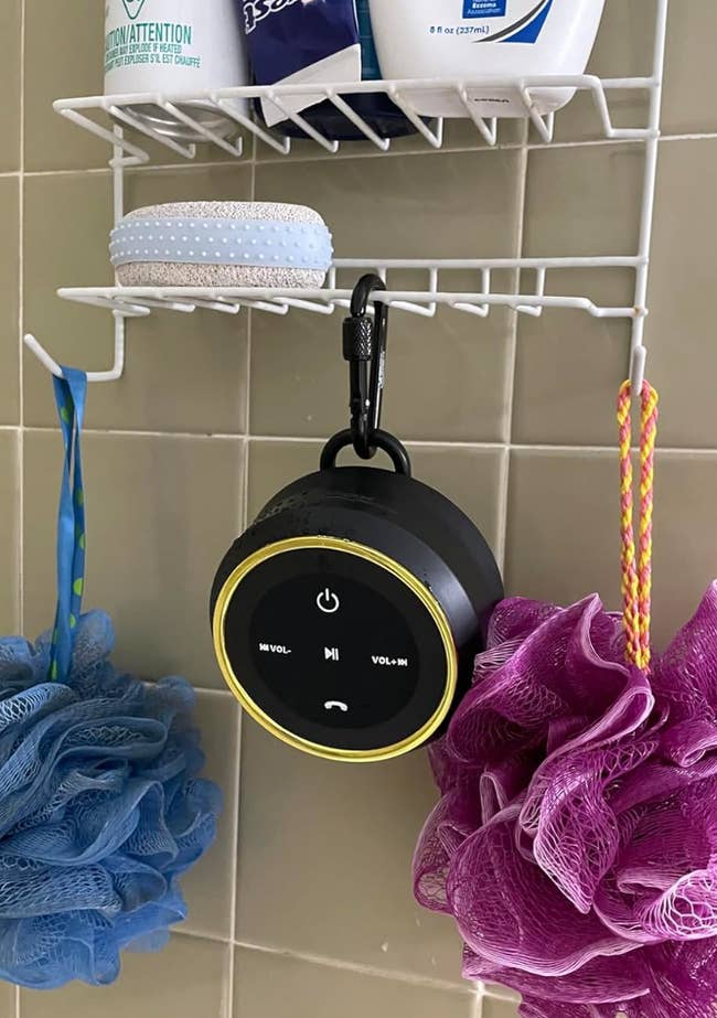 Round black waterproof speaker hanging in a shower caddy 