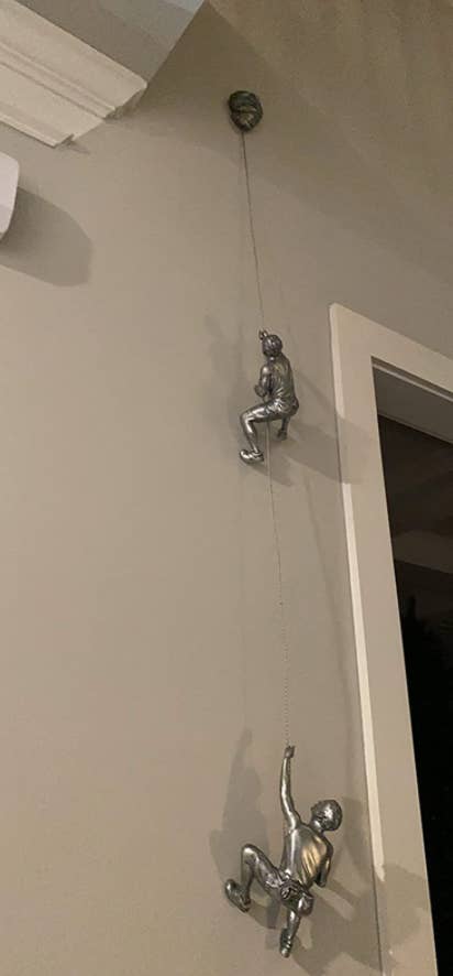 two silver tone people figurines that look like they're climbing up the wall