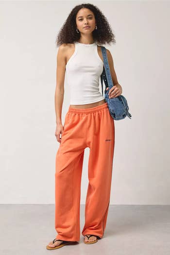 Model successful  vessel  top, orangish  sweatpants, and flip-flops holds denim enarthrosis  bag. Casual manner  benignant   suitable for shopping