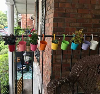 Assorted colorful planters hung on balcony railing, offering apartment gardening ideas