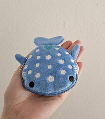 Plush blue coin purse shaped like a whale shark, held in an open hand, showing a zipper and keychain attachment