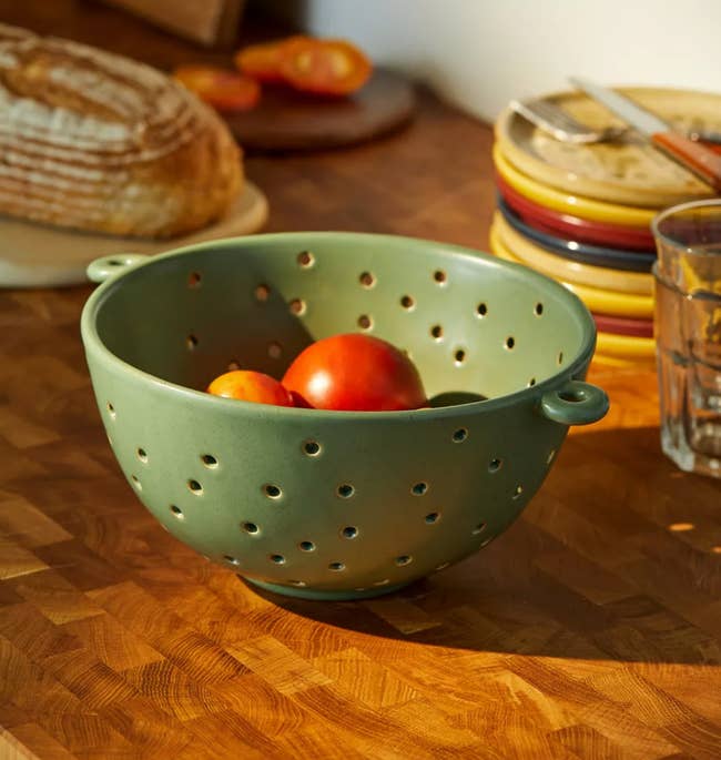 A green ceramic colander with little random holes in it 