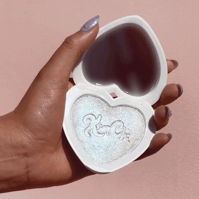 Heart-shaped compact with shimmering highlighter held successful  hand, lid unfastened  displaying embossed logo, perfect  for adding glow to constitution  routines