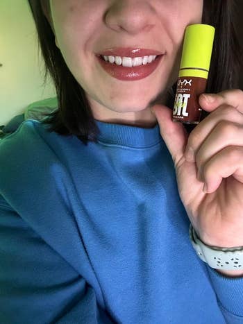 another reviewer holding a NYX Butter Gloss lip oil while wearing it
