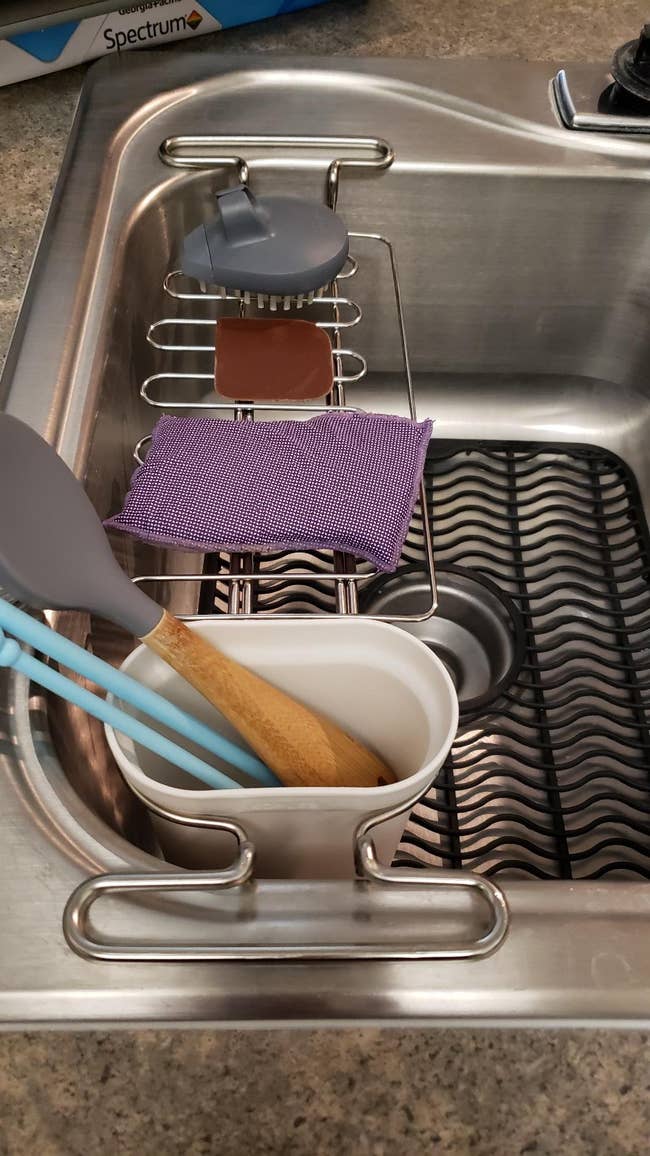 reviewer photo of the rack with a cleaning brush on it, bar of soap, sponge, and inside the soaking dish are two straws and a spoon