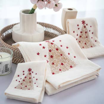 Elegant towels with intricate holiday tree embroidery, arranged beside a candle and flowers, suitable for festive shopping articles