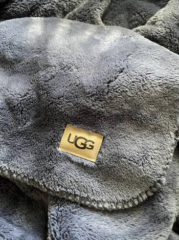 Close-up of a plush UGG blanket, showcasing its brushed  texture and logo. Perfect for cozy buying  needs