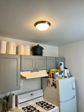 Kitchen with gas stove, cabinets, paper towels, and items on the fridge including a water bottle, coffee maker, and various boxes and containers