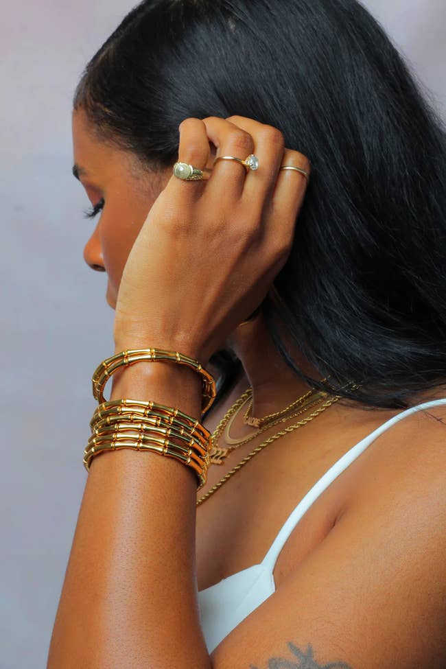 bracelets, rings, and necklaces, with a sleeveless top. They're adjusting their hair, showcasing the accessories
