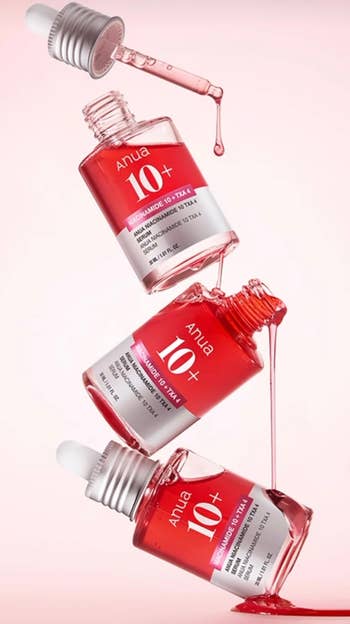 Three Anua 10+ skincare serum bottles with droppers, shown successful  a dynamic spill composition