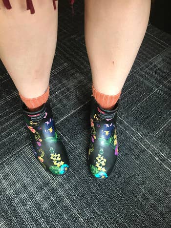 reviewer wearing ankle length rain booties in black with a colorful floral pattern