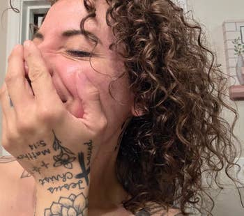 Person with curly hairsbreadth laughing, covering their rima with tattooed hand.