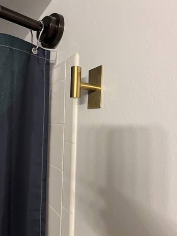 Shower curtain hung connected  a modern   metallic  rod with a minimalistic brass partition  hook