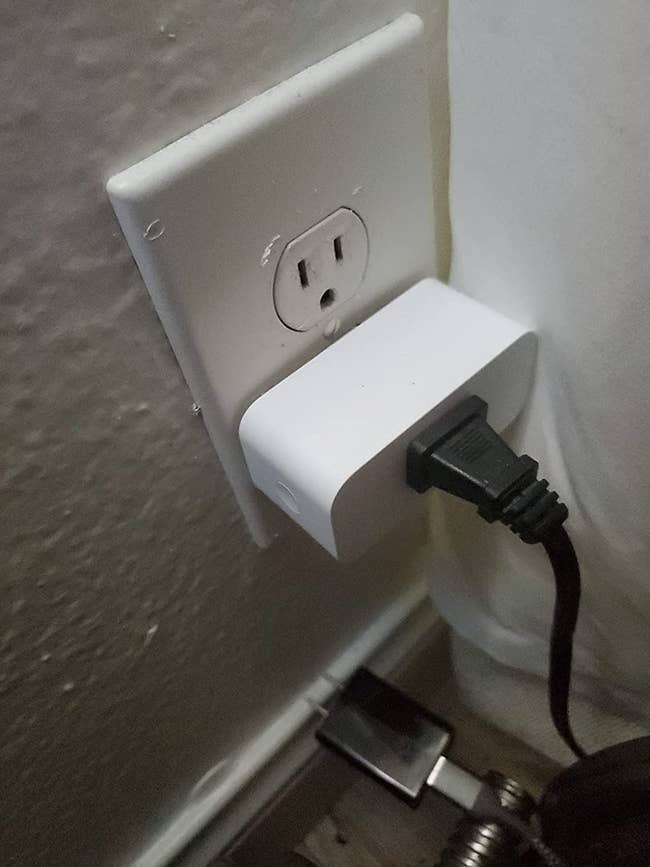 Reviewer's smart plug in the wall with a cord plugged in to it